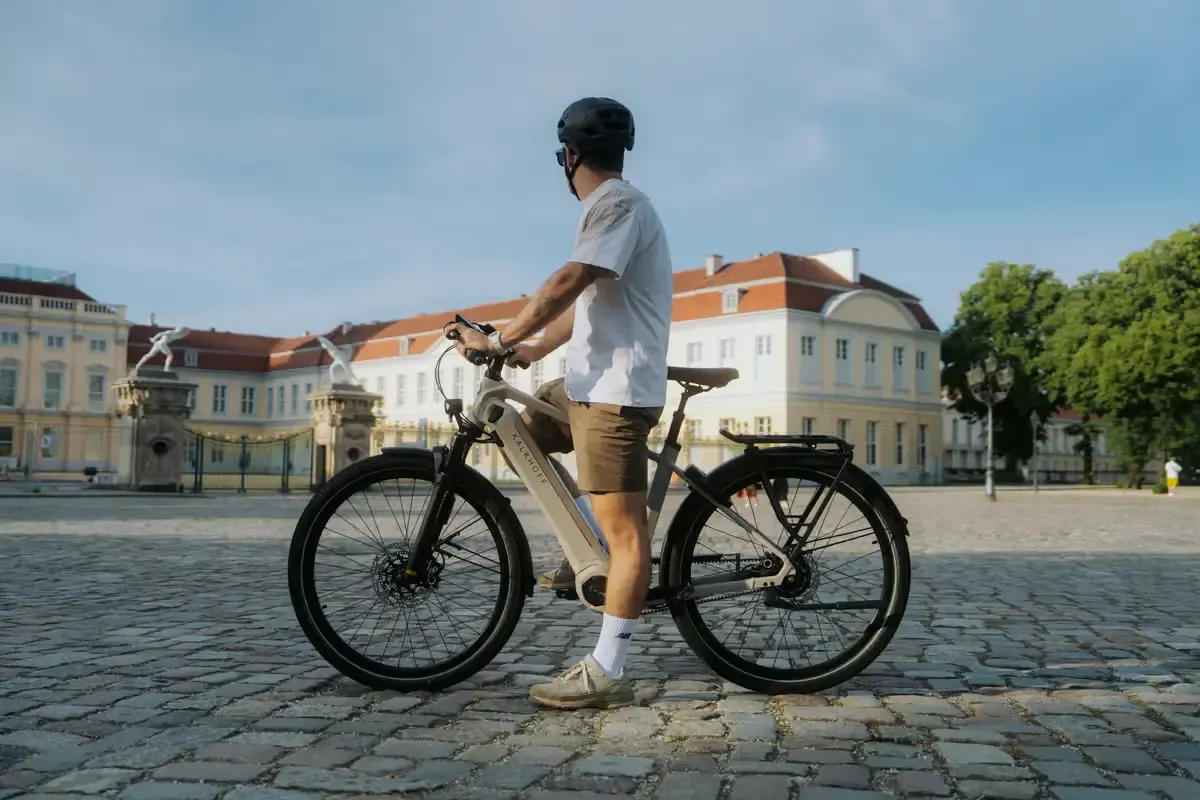 Man standing with bike on Plaza in front of building and looking away from the camera