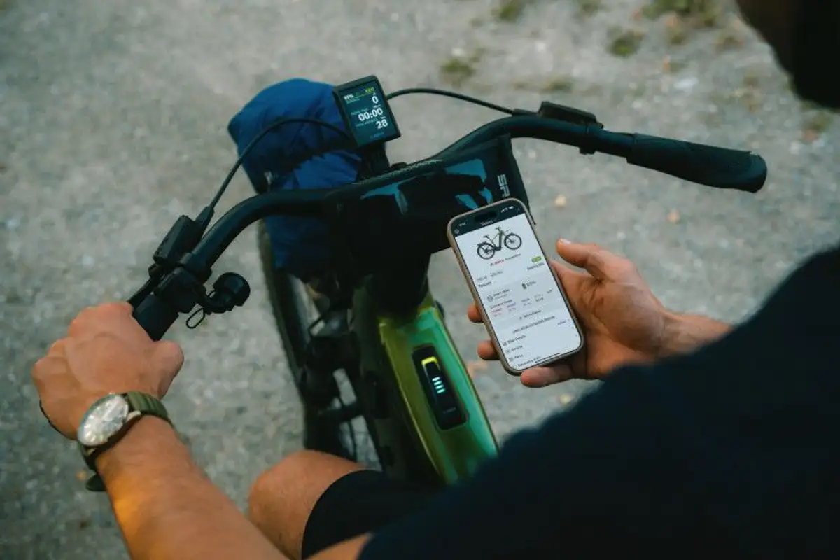 Mann sitzt auf Fahrrad und schaut auf sein Handy, eine Hand am Lenker, Detailaufnahme von oben