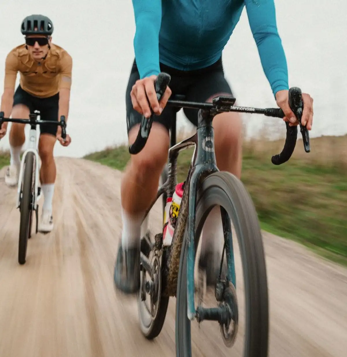 zwei Personen in sportlicher Kleidung auf Gravelbikes fahren hinter- und nebeneinander auf sandigem Weg
