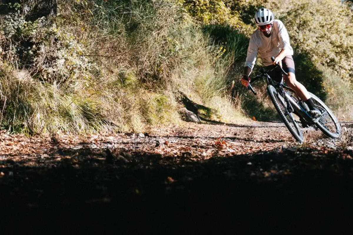 A male cyclist descends a winding dirt path through lush green foliage.