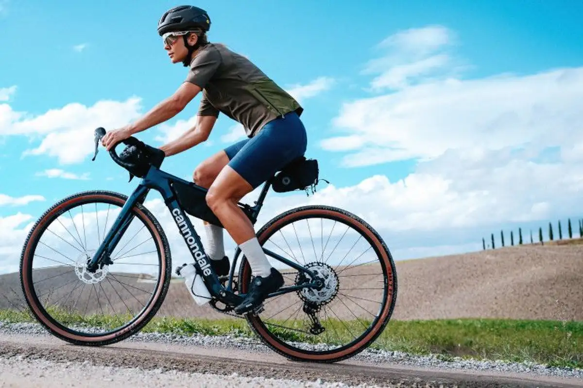 Person in sportlichen Klamotten auf Cannondale Rennrad vor blauem Himmel mit Wolken
