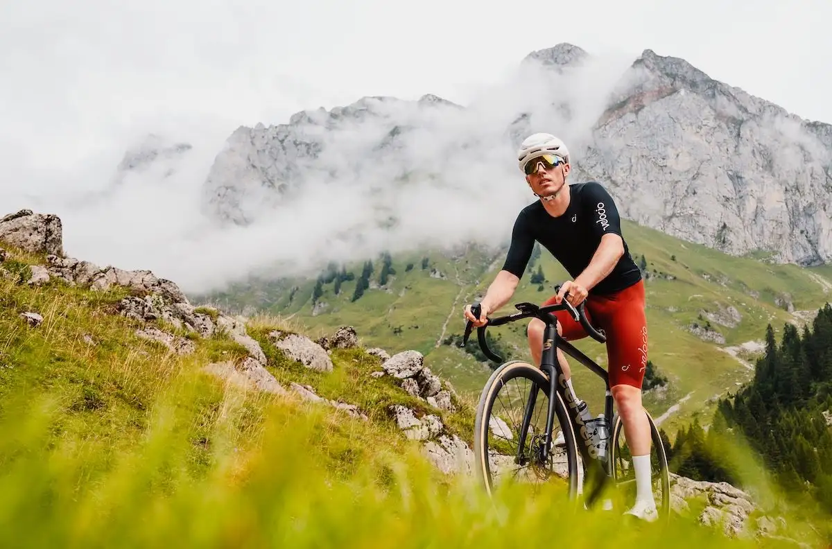 Man in red shorts and black shirt cycling a road bike uphill in foggy mountains.