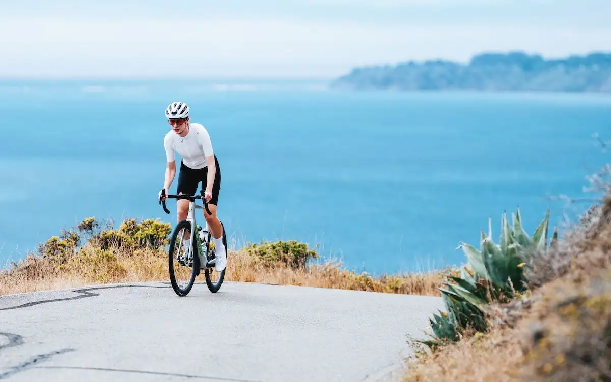 Person auf Gravelbike auf Straße, im Hintergrund das Meer