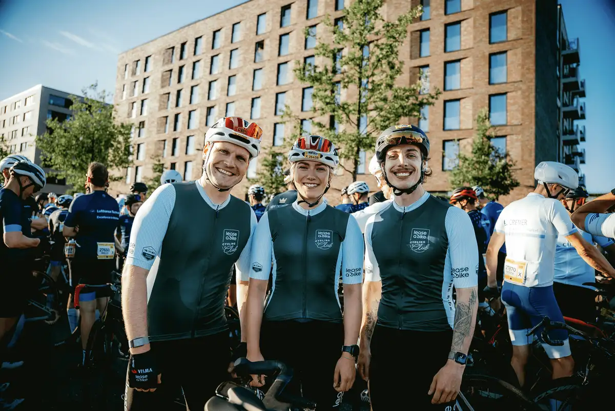 Drei Rennradfahrer des Lease a Bike Cycling Clubs stehen am Start eines Rennens und lächeln in die Kamera