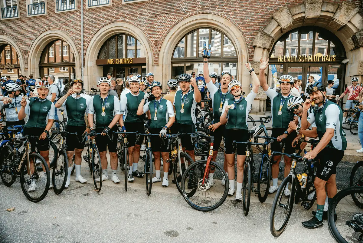 Eine Gruppe Radfahrer vom Lease a Bike Cycling Club jubelt vor einem Gebäude