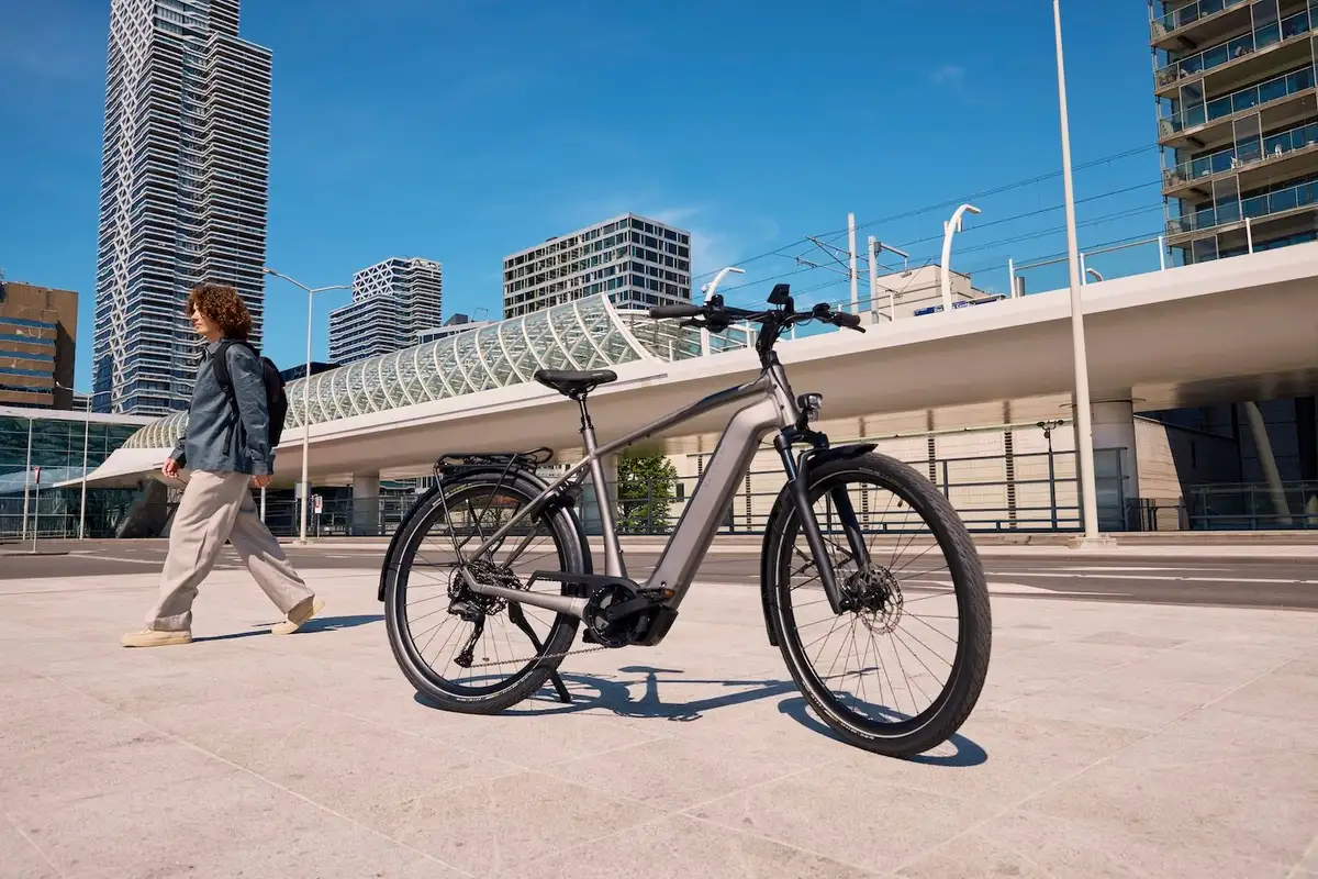 Mann geht im Hintergrund nach links, vorne steht ein graues Kalkhoff E-Bike, urbane Stadt im Hintergrund