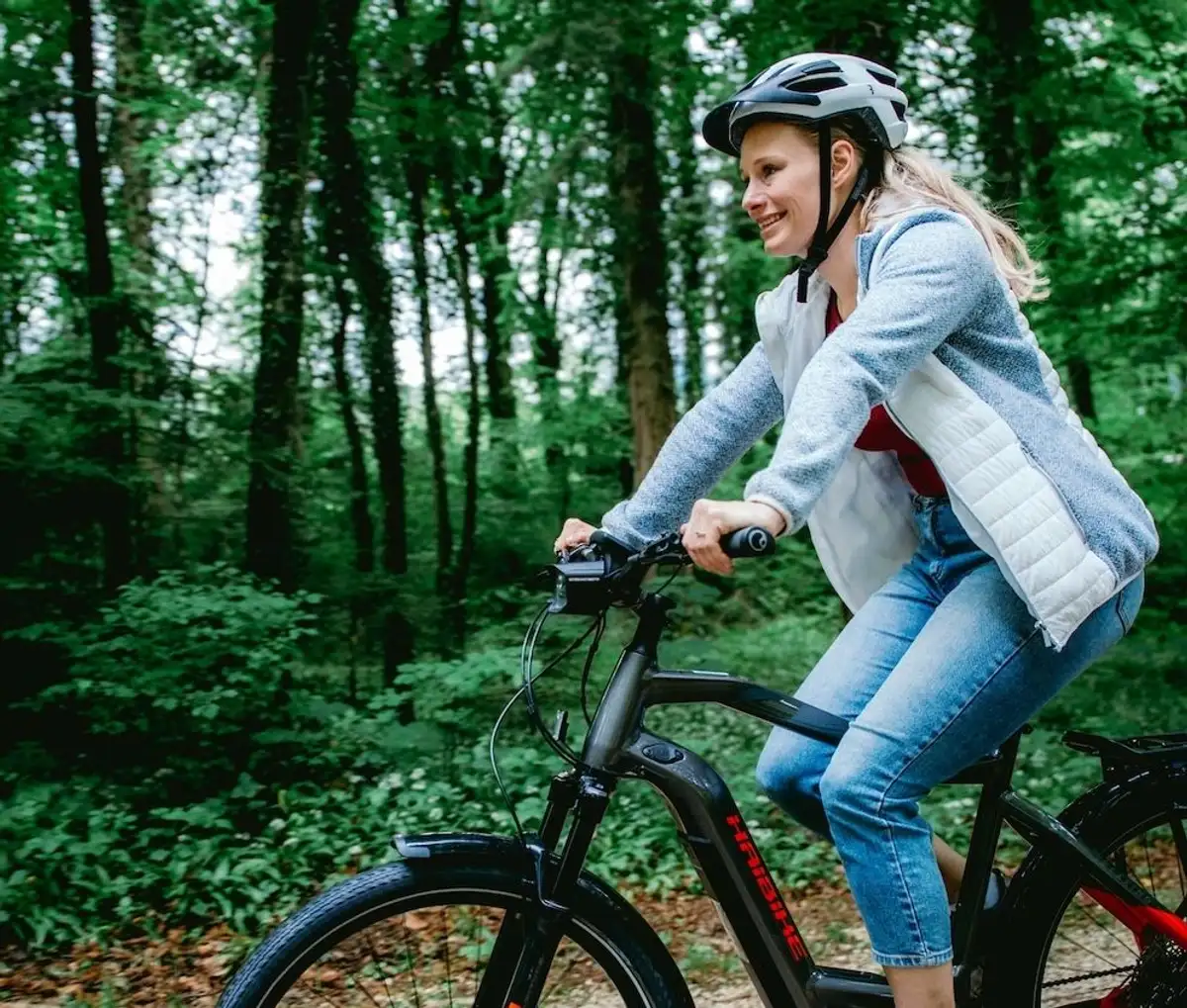Frau mit helm fährt lachend durch grünen Wald auf dem Fahrrad
