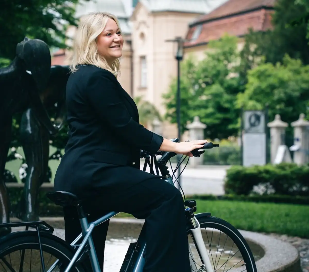 blonde Frau sitzt lachend auf E-Bike in städtischer Kulisse und schaue nach rechts