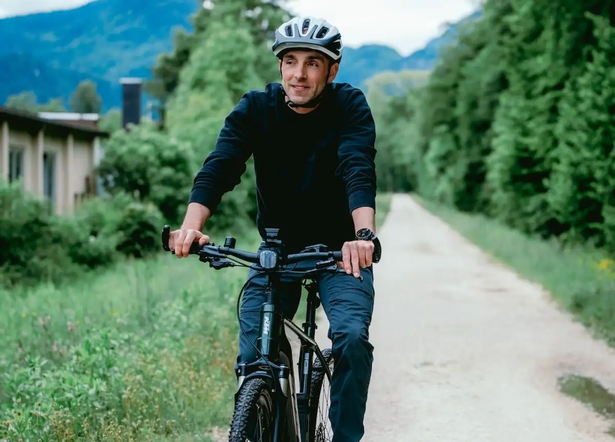 Mann fährt mit Fahrrad auf Radweg in grüner Umgebung und bergiger Landschaft im Hintergrund
