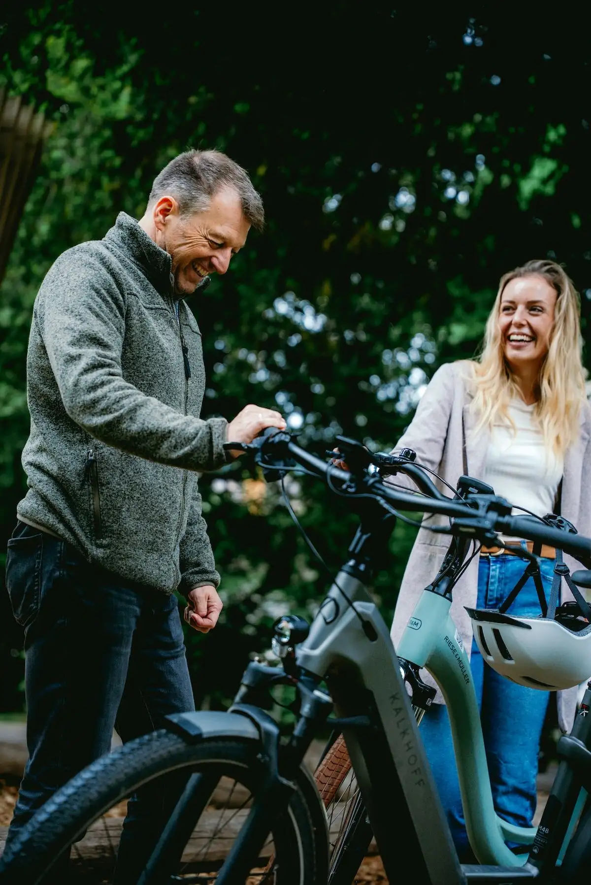 Älterer Mann und jüngere Frau stehen neben ihren E-Bikes und lachen gemeinsam
