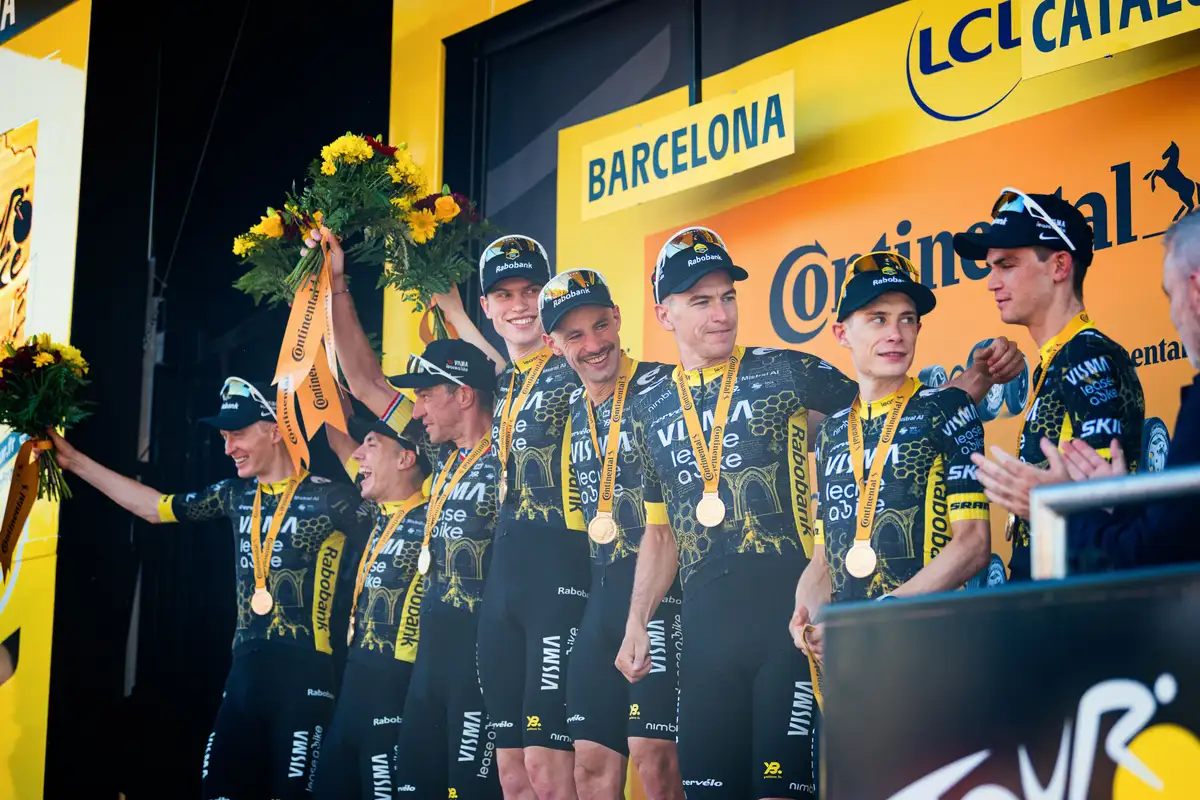 Victorious cycling team in black and yellow uniforms on a podium with medals and flowers.