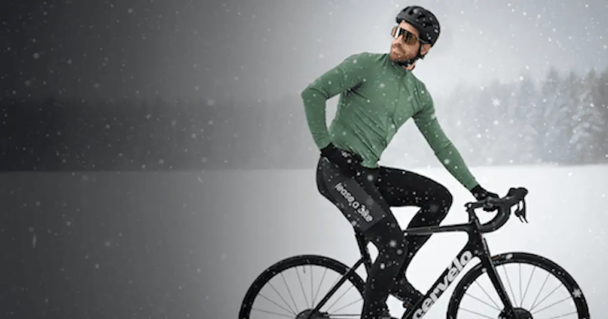 Mann in Radfahrerkleidung fährt mit einem Rennrad durch eine verschneite Landschaft.
