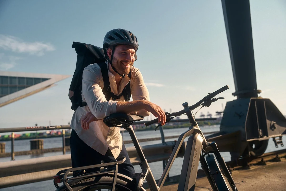 Mann mit Helm und Rucksack lehnt auf Sattel seines E-Trekkingbikes und lacht