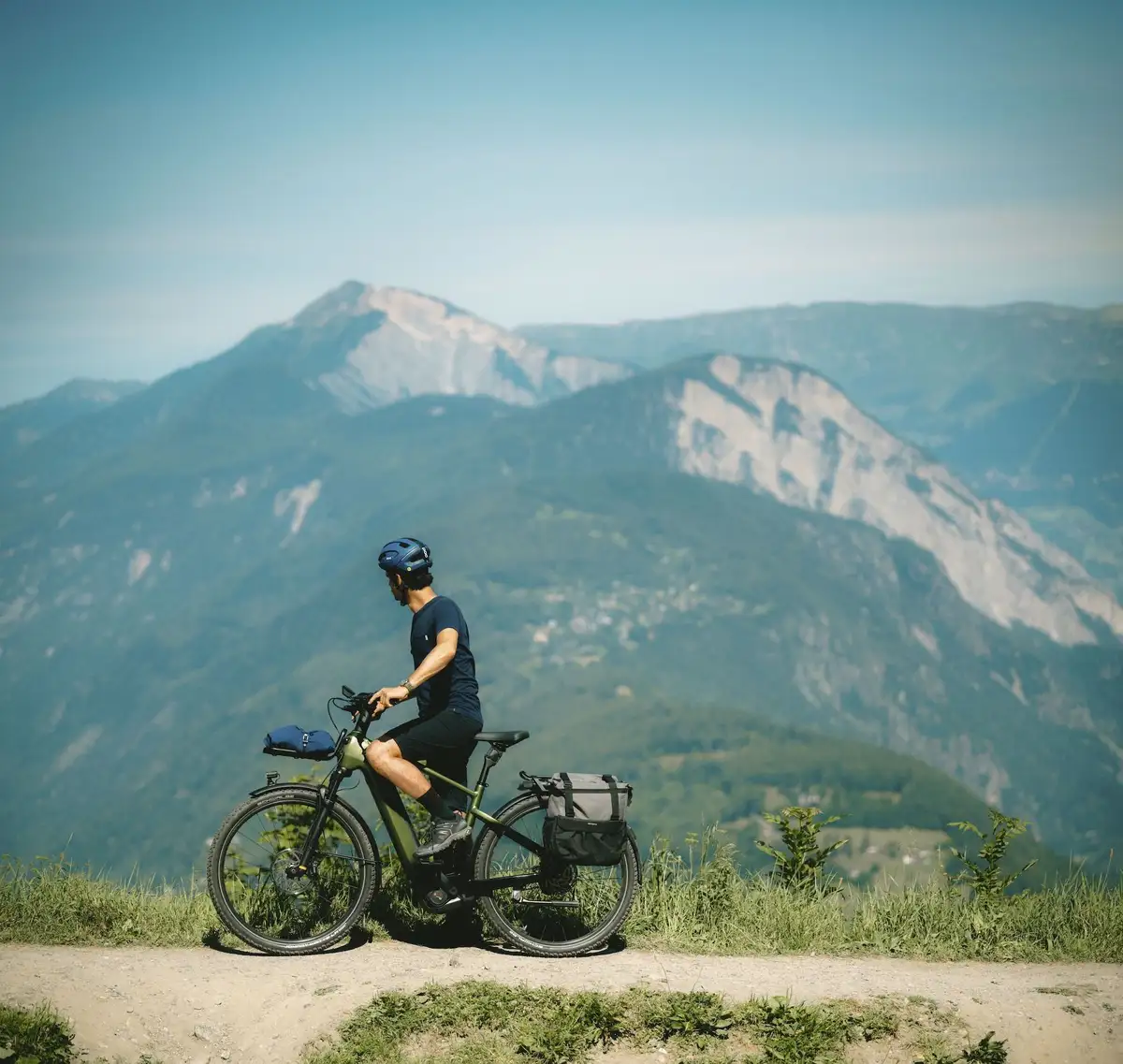 Mann steht mit Bike vor Bergkulisse und guckt ins Tal