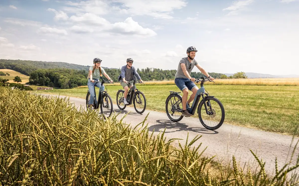 Drei Personen fahren Fahrrad in hügeliger Landschaft