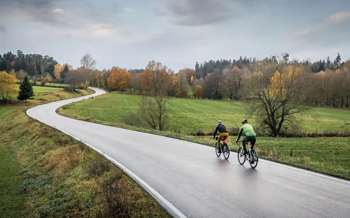 Zwei Radfahrer fahren auf nasser Straße inmitten von grüner Landschaft