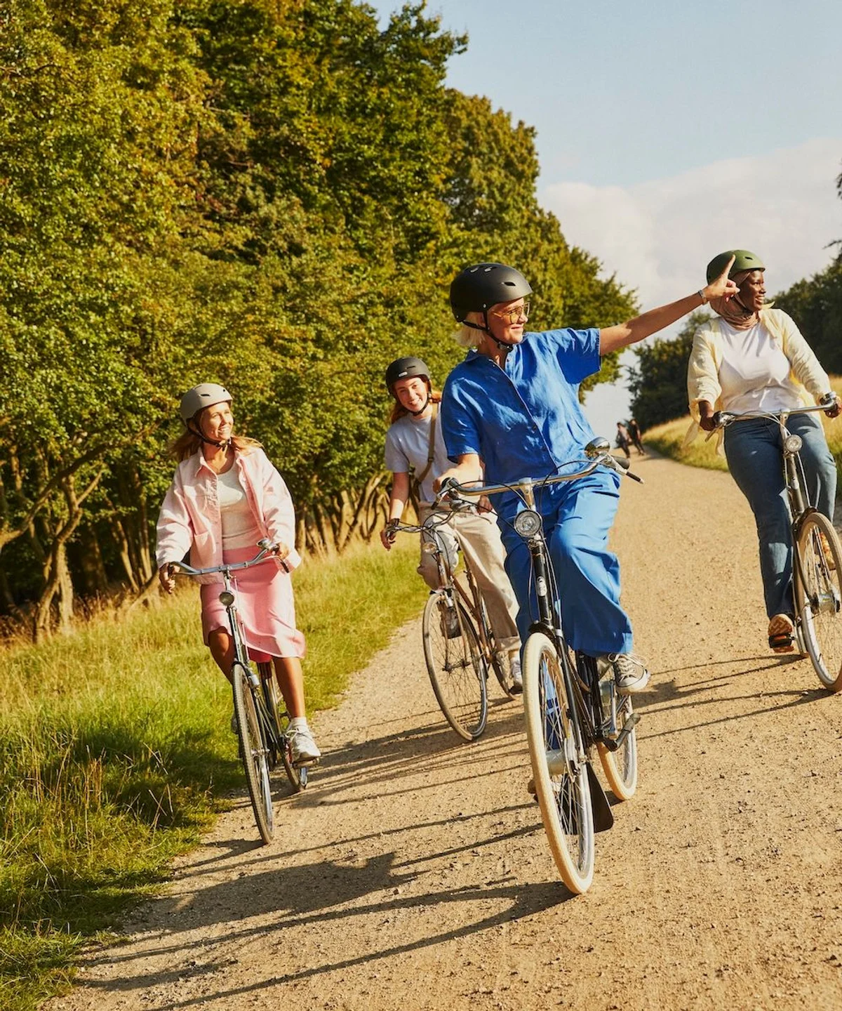 Gruppe aus vier Person fährt lachend mit Citybikes über Schotterweg, eine Person zeigt nach rechts
