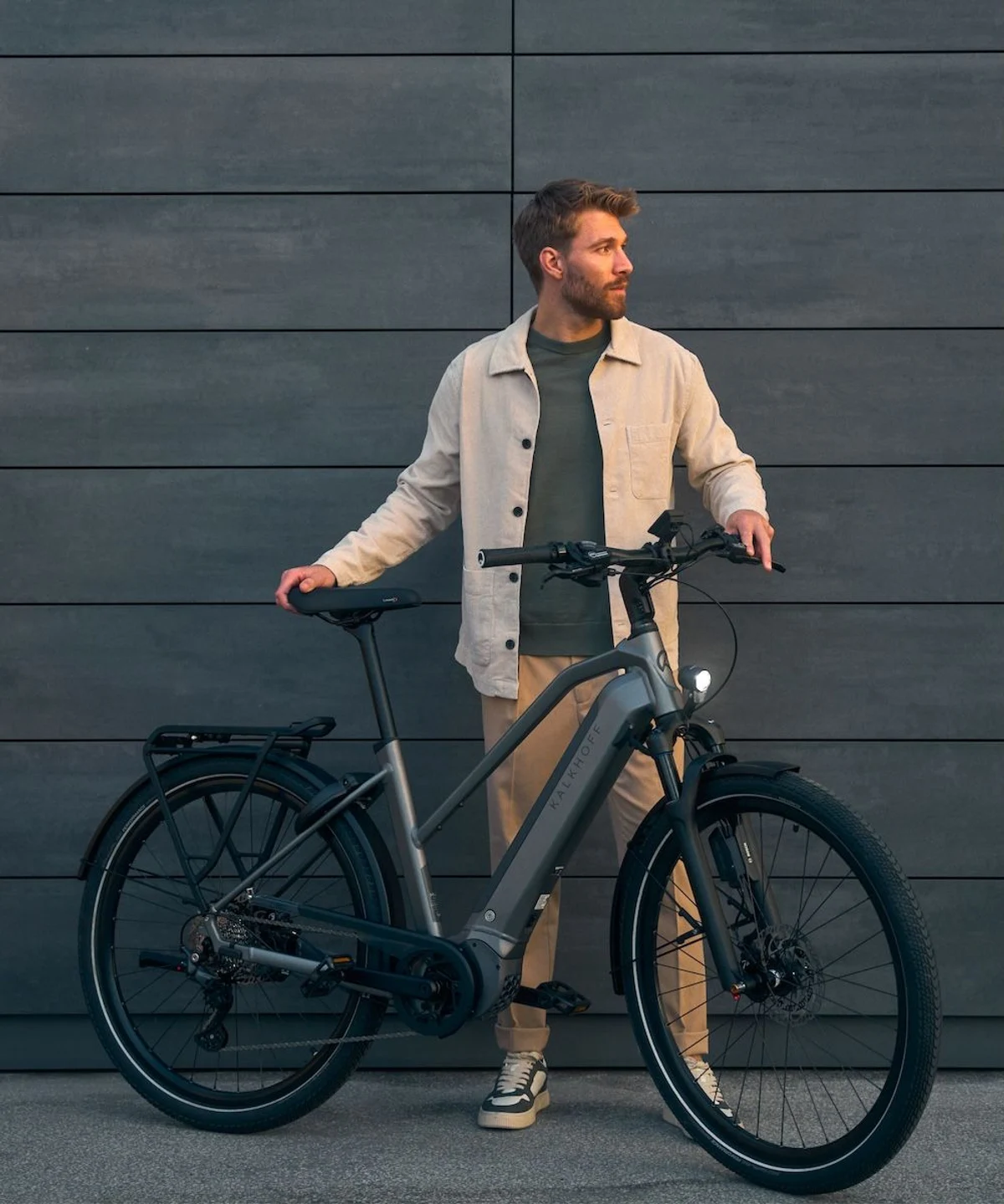 Mann steht mit E-Bike in urbaner Umgebung, lehnt sich auf Sattel und schaut in die Ferne