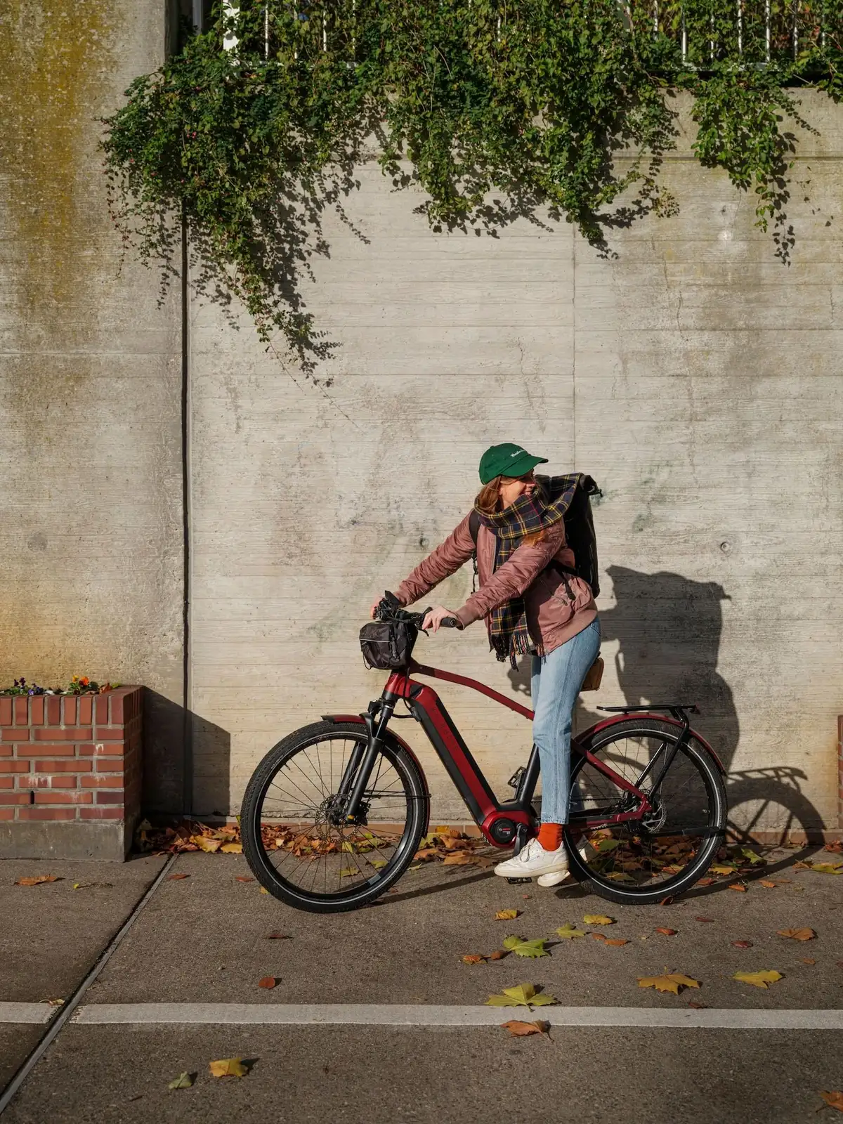 Frau auf Kalkhoff Fahrrad und herbstlichem Outfit steht vor Mauer und schaut nach hinten