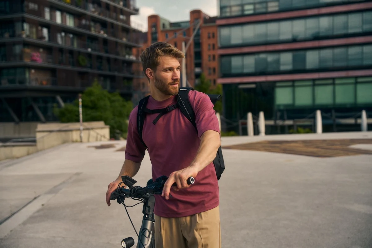 Mann schiebt Fahrrad vor Häusekulisse und schaut nach rechts