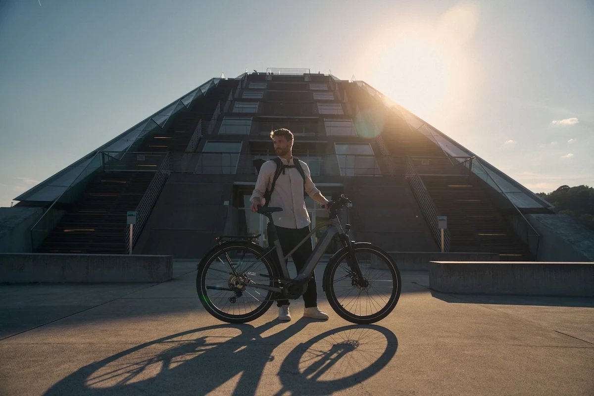 Mann mit Kalkhoff Fahrrad steht vor Gebäude, Sonne im Hintergrund