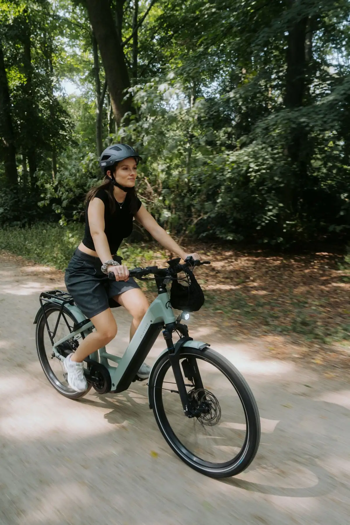 Frau mit Helm in Sommerkleidung auf E-Bike in Wald