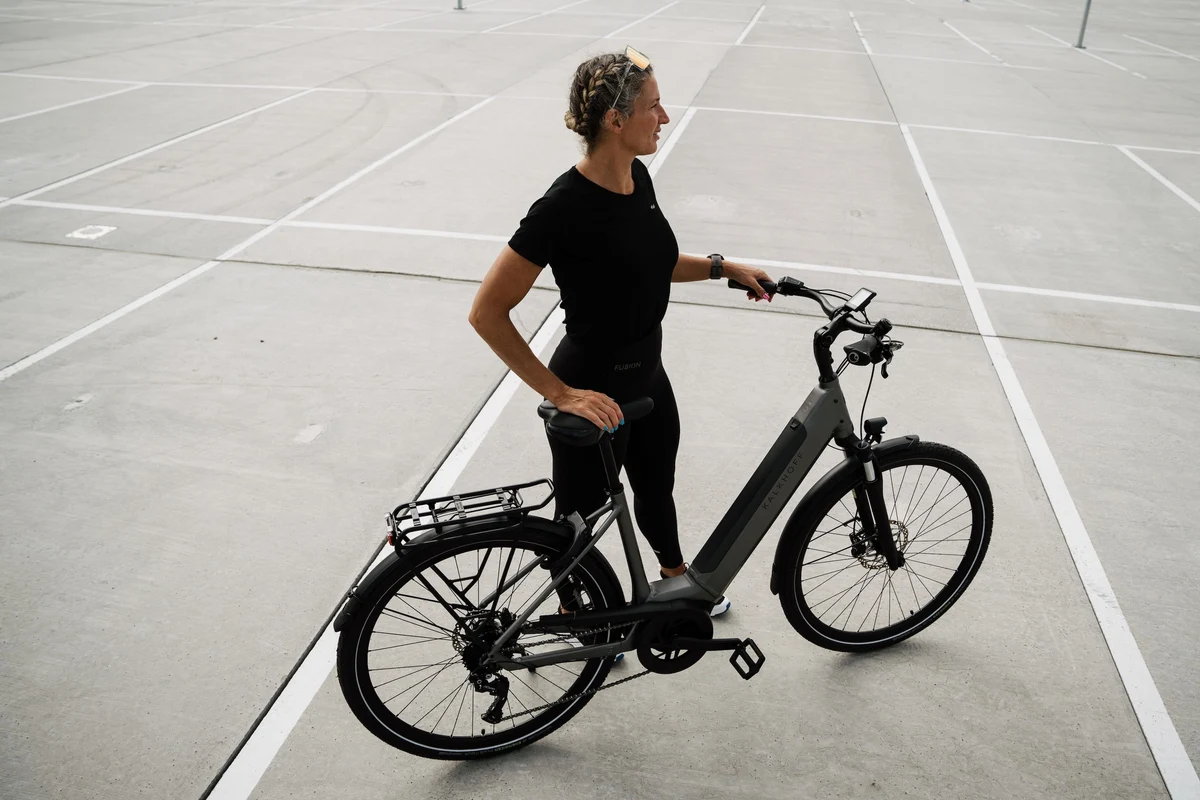Frau steht mit Kalkhoff Fahrrad auf Betonfläche und schaut nach vorne