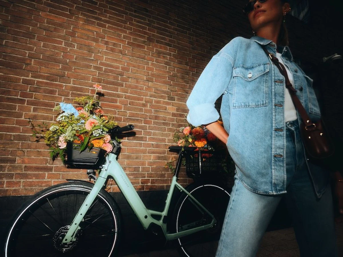 Kalkhoff Fahrrad Frau mit Blumen im Korb steht vor Mauer