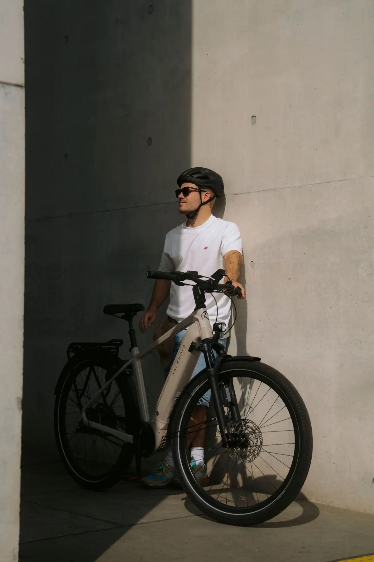 Mann lehnt mit E-Bike an Betonwand und genießt die Sonne