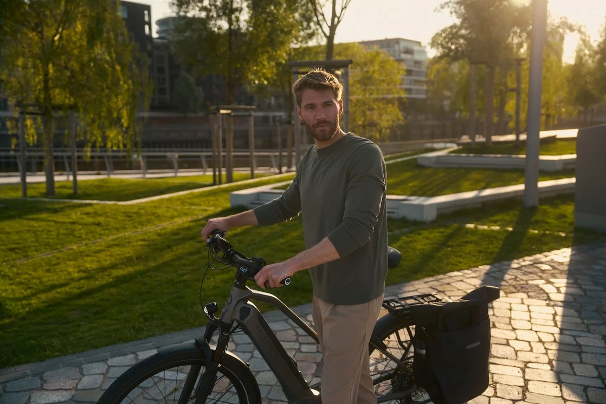 Mann schiebt E-Bike durch sonnigen Park und schaut nach links