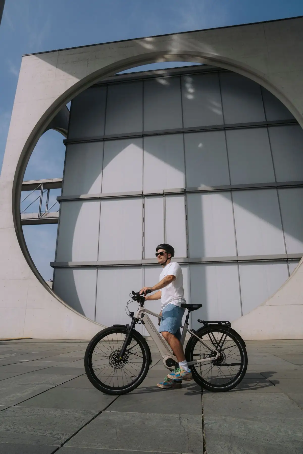 Mann steht mit E-Bike im Sommer vor Gebäude und blickt in die Ferne