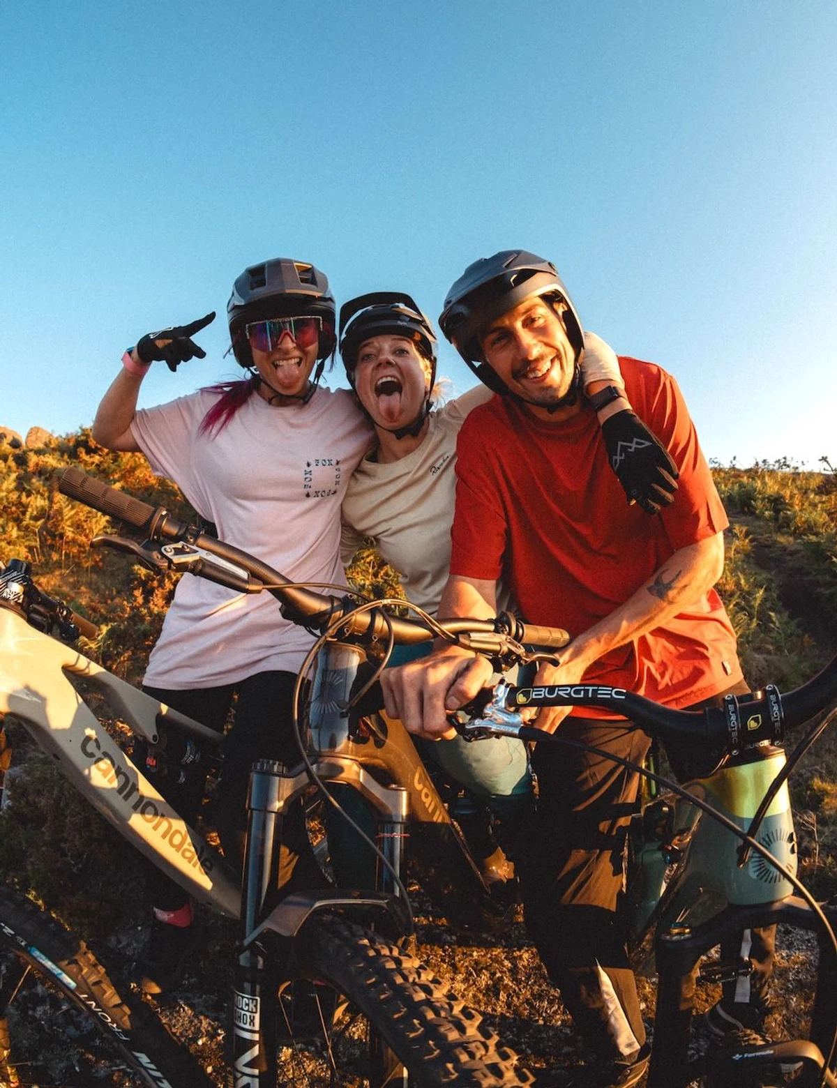 drei Personen mit Mountainbikes liegen sich lachend in den Armen und grinsen in die Kamera
