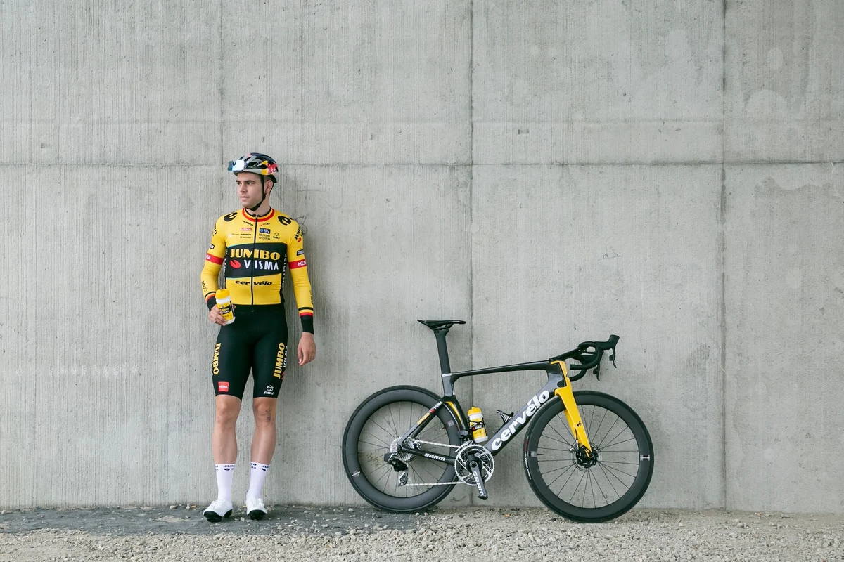 Team Jumbo-Visma Radfahrer in Teamkleidung lehnt an Betonwand neben Rennrad
