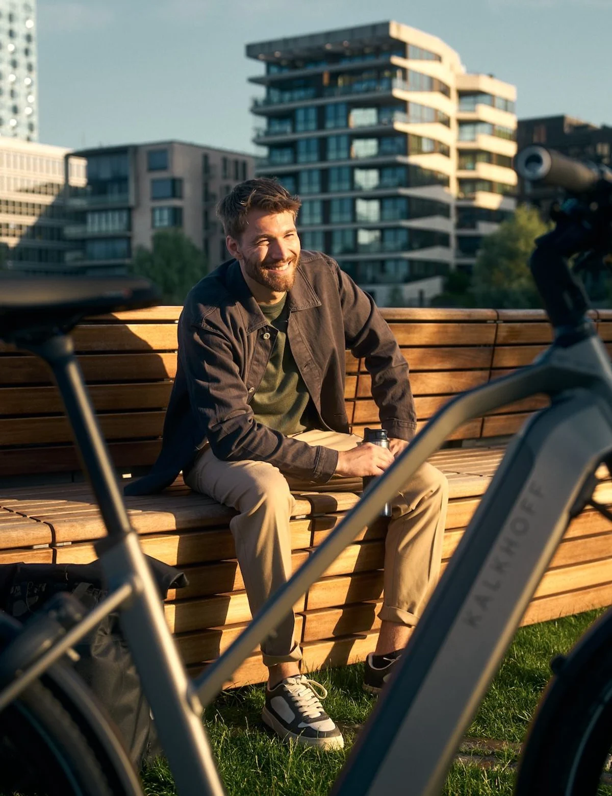 Mann sitzt lachend auf Bank und davor parkt ein Kalkhoff E-Bike