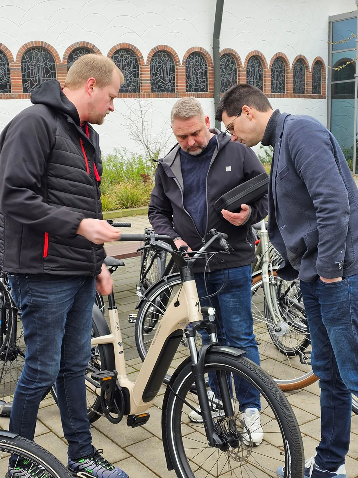 Drei Personen begutachten gemeinsam ein E-Bike im Außenbereich