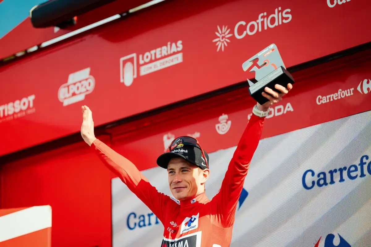 Jonas mit Trophäe und rotem Trikot auf Podium streckt beide Arme hoch