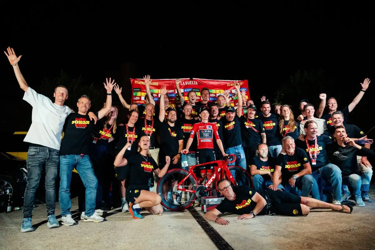 A large group of people in matching t-shirts celebrate with a race car.