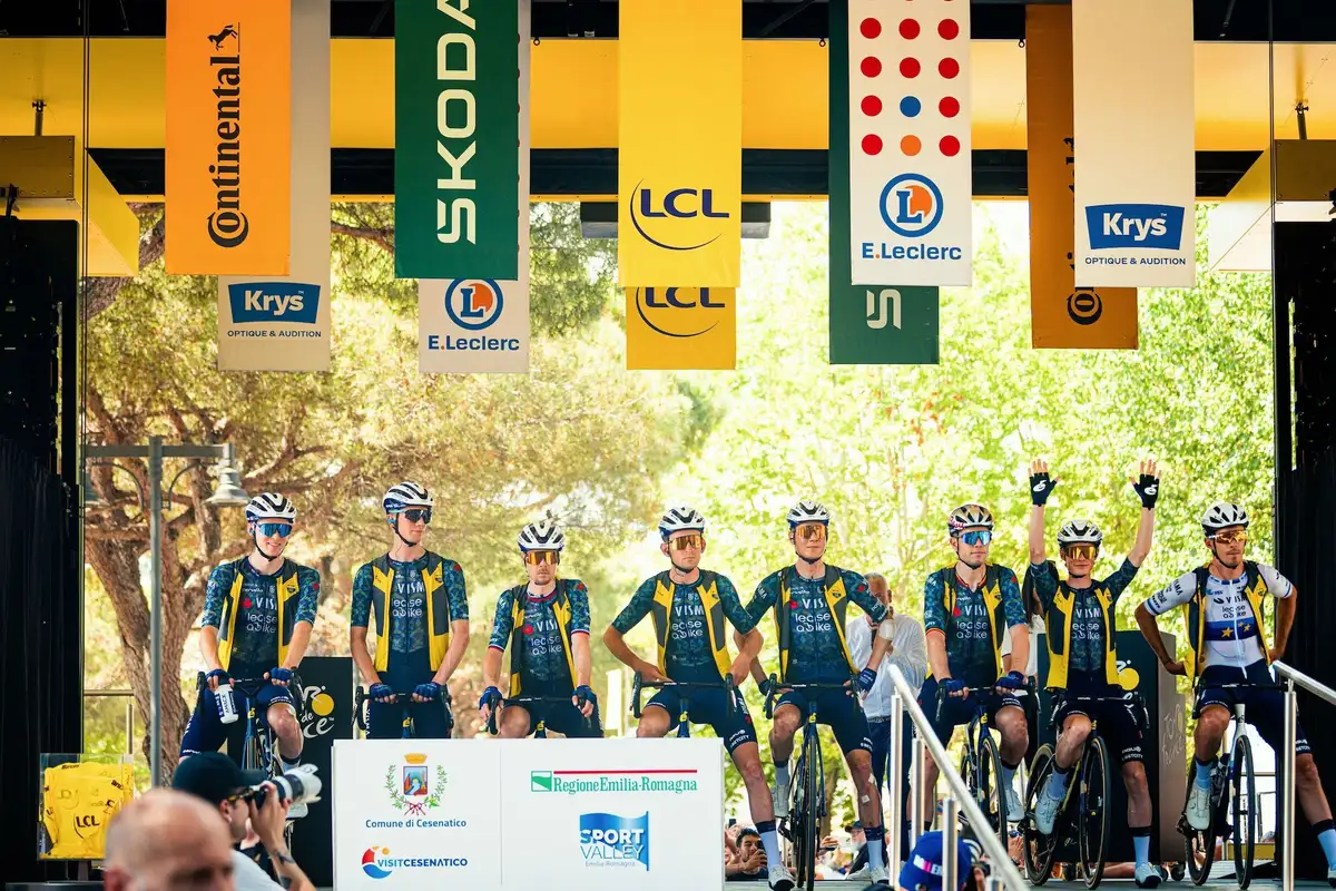 Cycling team on stage in front of sponsor banner during team presentation
