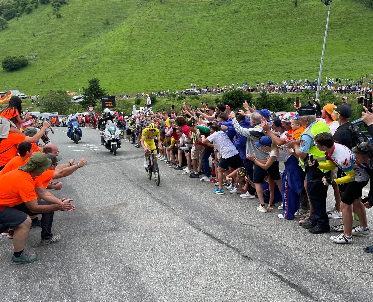 Professional cyclist rides mountain stage with cheering spectators lining the route
