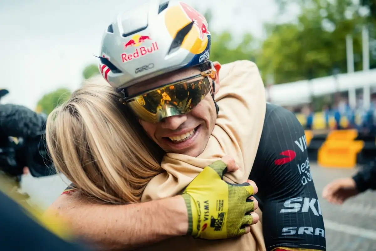 Cyclist Wout van Aert wearing a Red Bull helmet embraces a woman after a race, both smiling warmly.