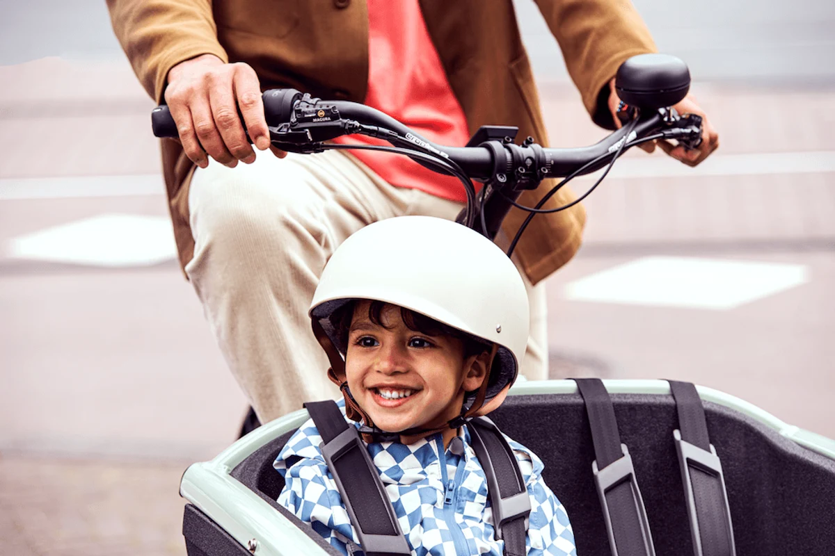 Kleiner Junge mit Helm sitzt lachend im Lastenrad